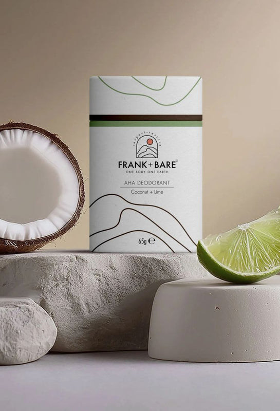 All Natural deodorant tube made from cardboard, AHA Deodorant Coconut + Lime standing on a white stone with a coconut and lime wedge next to it with a pale background